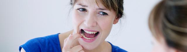 femme qui inspecte ses dents dans un miroir pour prévenir les premiers signes de maladie des gencives