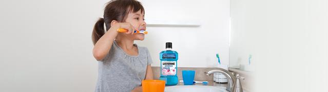 petite fille se brossant les dents, avec un flacon de rince-bouche Listerine sur le comptoir